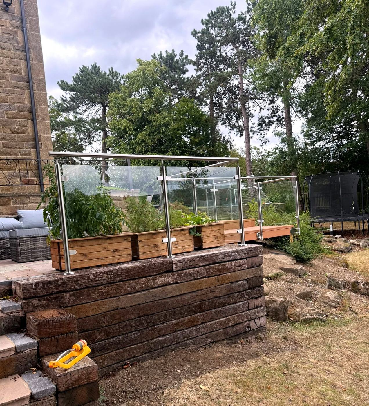 Glass balustrade base-fixed on top of a timber sleeper retaining wall beside stone steps, Sheffield S17